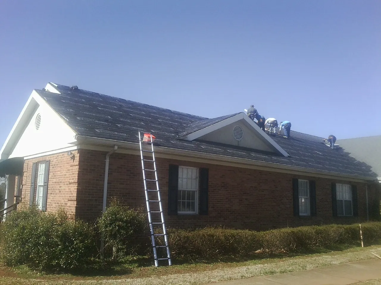 Crew tearing shingles off a brick ranch roof with a ladder set — Emergency Roof Repair work by our crew in Keymar