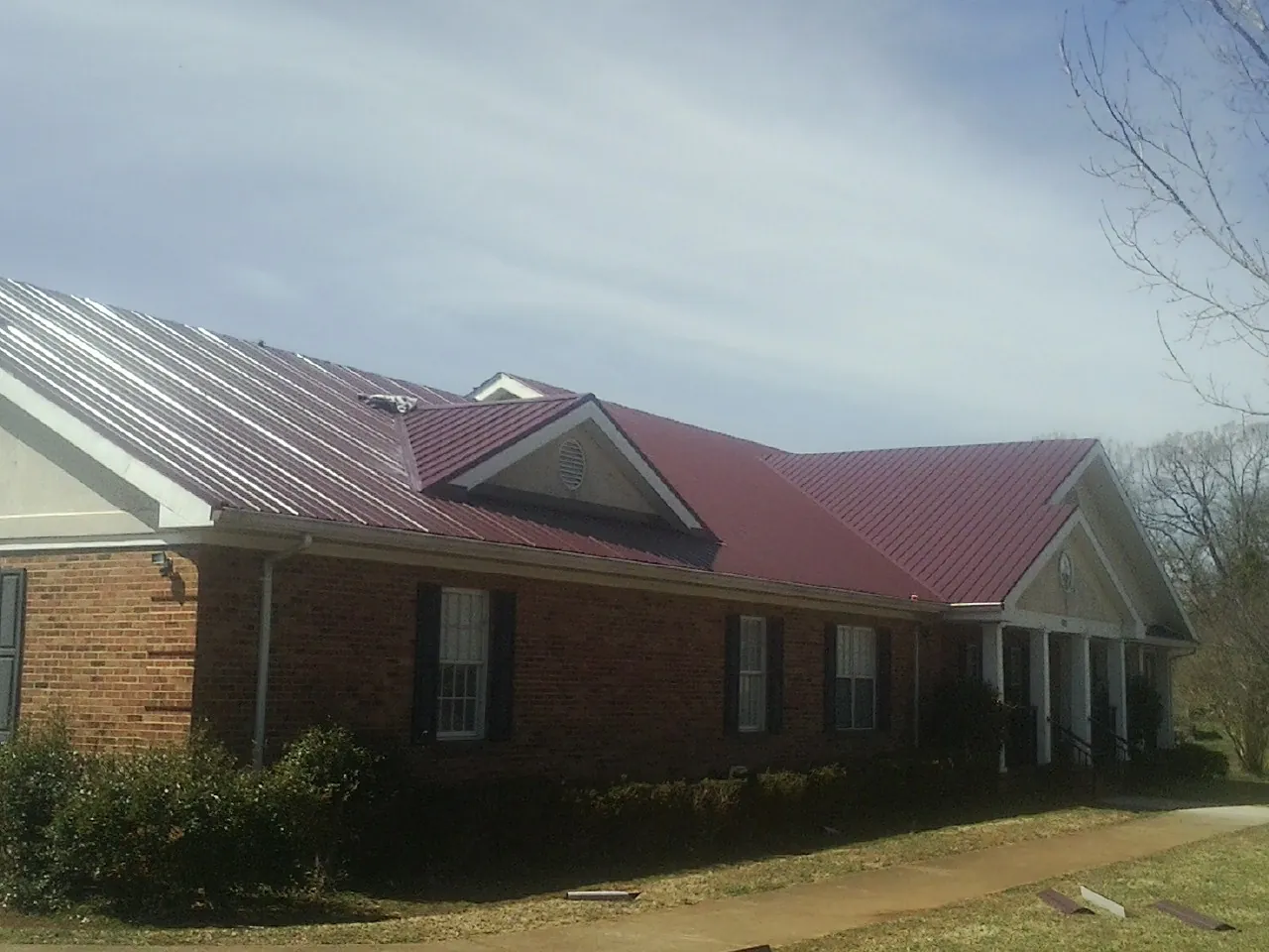 Red metal roof with gabled entries on a long brick building, from a Hail Damage Roof Repair job in Keymar