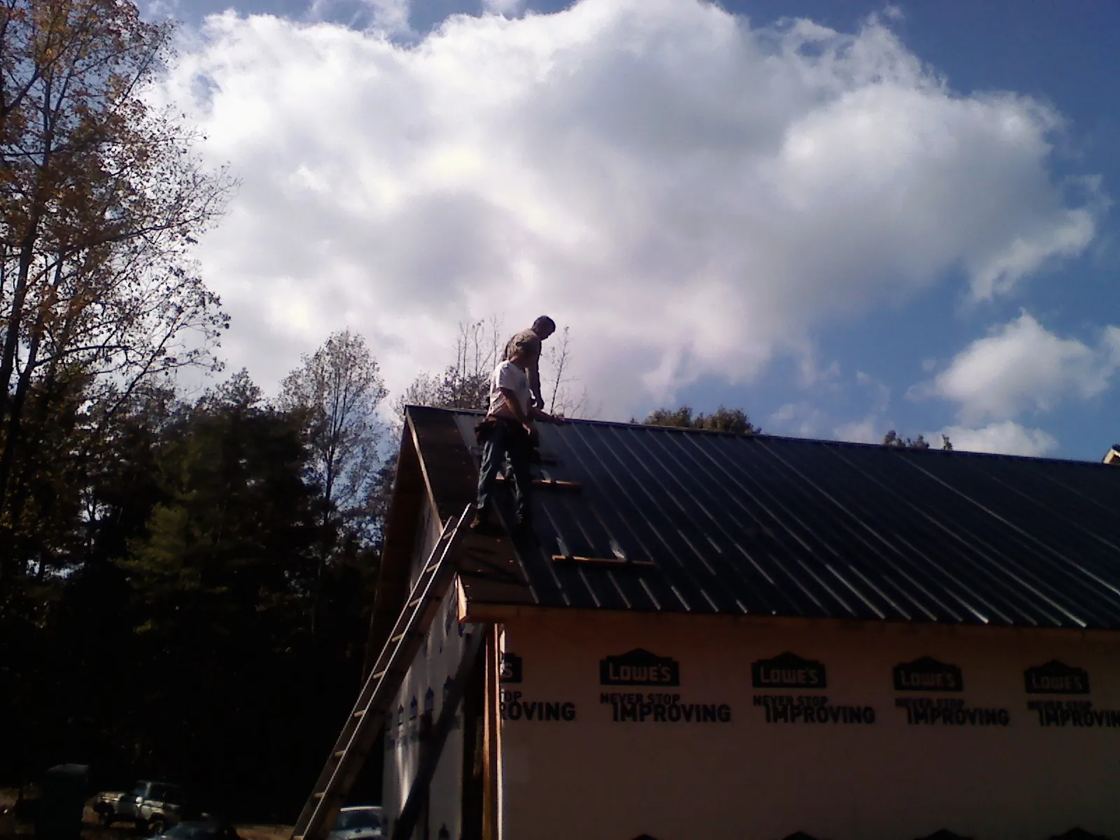 Roofer fastening dark metal panels high against a cloudy sky, from a Roof Inspection job in Keymar