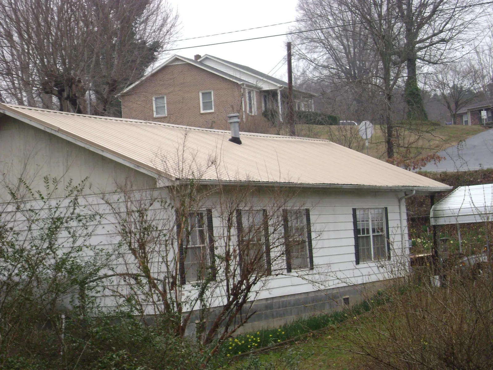 Tan metal roof on a white sided house set into a hillside — Commercial Roofing by Roofing Brothers in Keymar